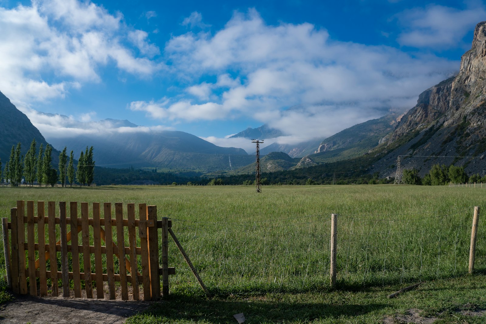 Portón de madera y campo verde con cordillera al fondo